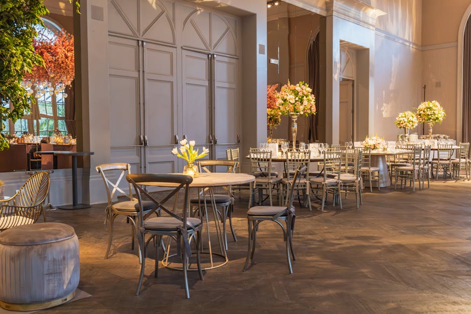 An elegantly decorated event space featuring round tables and chairs arranged for a formal gathering at Morden Hall Park. Each table is adorned with a tall glass vase holding a lush floral arrangement