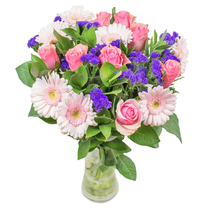 Displayed in a flawless clear glass vase against a radiant white background, this vibrant bouquet encapsulates the essence of Merton's floral spirit. The centrepiece showcases roughly seven to nine medium-pink roses, their petals pinpointing the transition between tight buds and blooming fullness, exuding classic romance. Alongside, five to seven pale pink gerbera daisies display broad, ruffled petals and softly lit, nearly white centres-like fresh morning blossoms glimpsed in Morden Park. Scattered among the blooms are hand-gathered clusters of bright, vivid purple statice, lending both contrast and textural intrigue. Rich, deep green foliage brings a lush fullness and a scent evocative of local English gardens, grounding the arrangement. The visible stems and water in the transparent vase underscore the freshness and attention to detail you'd expect from a skilled Merton florist. This charming assortment, perfect for birthdays, anniversaries, Mother's Day, or simply brightening a Colliers Wood kitchen, radiates joy, celebration, and sincere affection.